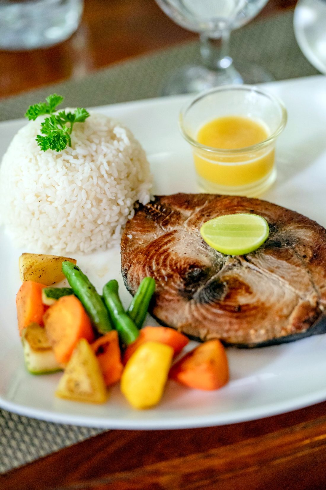 A grilled tuna steak with rice, lime and vegetables on a white plate